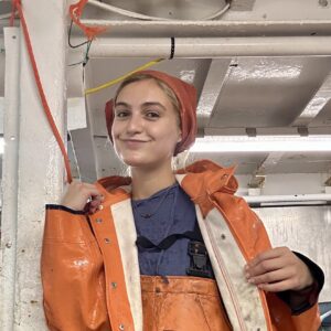 A person wearing a hat and waterproof clothes smiling while on a boat.