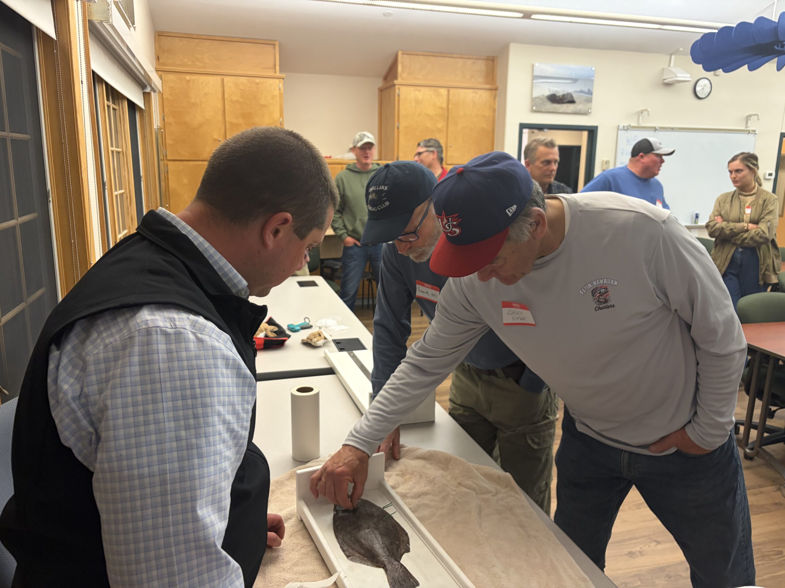 Three men looking at a green tag attached to a flatfish.
